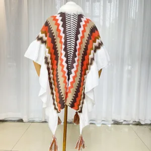 Knitted geometric chevron poncho cape with white faux fur collar and tassels detail view.