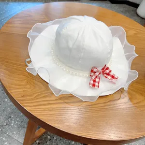 Detail view of a cute baby sun hat in white with pearl trim and a red checkered bow.
