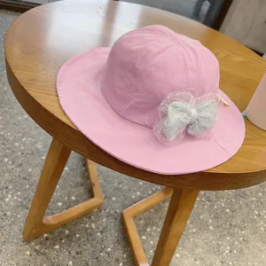 Detail shot of a cute pink baby bucket hat with a blue mesh bow on a wooden table surface.