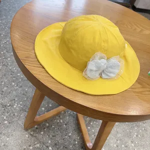 Cute yellow kids bucket hat with grey lace bow detail, perfect for spring sun protection.