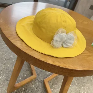 Yellow toddler bucket hat with grey lace bow detail, closeup shot on wooden table.