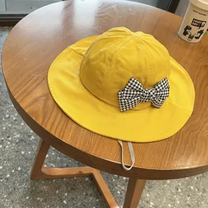 Detail view of cute yellow kids bucket hat with black and white houndstooth bow decoration.