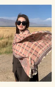 Outdoor scenic detail of a fashionable plaid fringed scarf worn by a woman in grassland.