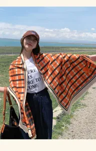Outdoor detail view of stylish orange plaid scarf and fashion cap worn by model in nature.