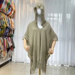 Close-up detail of knitted hooded poncho with fringe trim and wooden button closure design.