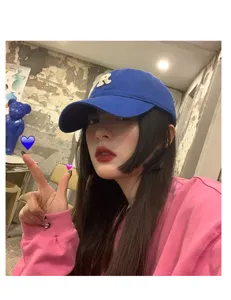 Detail view of a stylish blue baseball cap featuring a white R letter patch worn by a model.