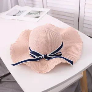 Pink straw sun hat detail, large brim with navy blue bow, perfect for summer beach and travel.