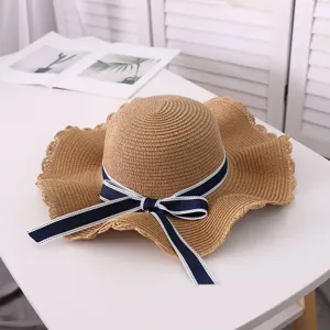 Close-up detail of the straw sun hat showing the delicate wavy brim and navy bow ribbon.