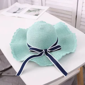 Detail view of a light green straw sun hat with navy blue bow ribbon on white table.