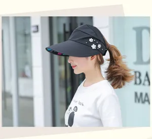 Detail view of a black empty-top sun visor with delicate pearl and floral decorations, worn outdoor.