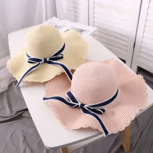Close up view of stylish summer straw sun hats with elegant navy blue bow ribbons on table.