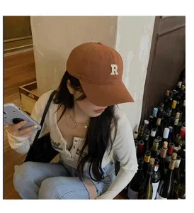 Gorra de béisbol marrón con bordado R, visera curva, detalle de estilo urbano retro.