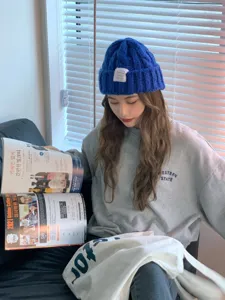 Detailed view of a soft blue knitted beanie hat worn by a model in casual outfit indoors.