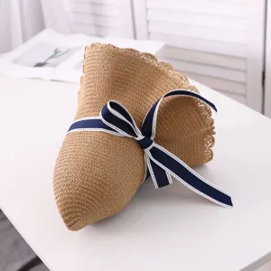 Close-up detail of the woven straw hat with elegant navy blue bow ribbon, perfect for summer.