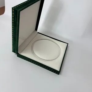Caja de joyería de terciopelo verde oscuro con borde dorado y interior blanco para anillos.