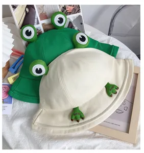 Close-up detail of cute frog bucket hats in green and white, featuring funny eyes and feet.