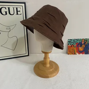 Detailed view of the brown pleated bucket hat on a wooden mannequin head display stand.