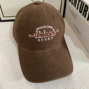 Detalle de gorra de béisbol de pana marrón con elegante diseño de letras bordadas y ala ancha.