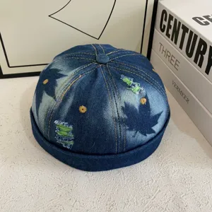 Gedetailleerd uitzicht van retro gewassen denim docker muts, versleten esdoornblad en groene rand.