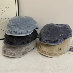 Gedetailleerd overzicht vintage gewassen denim krantenjongenspetten met metalen logo's.