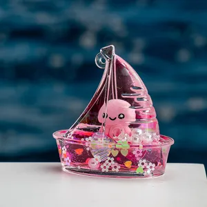 Joli porte-clés sable mouvant liquide en forme de voilier avec un pendentif pieuvre rose.
