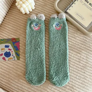 Detail view of cute green fuzzy plush floor socks featuring a funny cartoon one-eyed monster face.