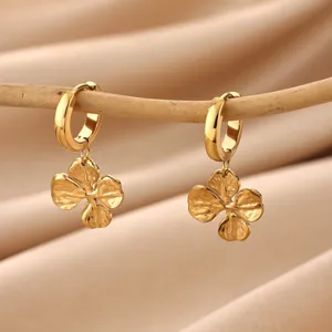 Close-up detail of exquisite gold four-leaf clover drop earrings hanging on a thin wooden stick.