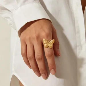 Close-up detail shot of a textured gold butterfly ring worn on a finger, elegant and chic jewelry.