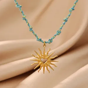 Close-up of gold sun heart pendant necklace with blue braided cord chain, detail view.