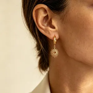 Close-up detail of a delicate gold hoop earring featuring a sunburst pendant with a heart.