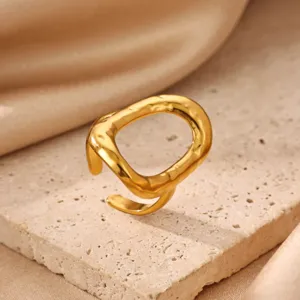 Detailed close-up of a stylish gold-plated irregular textured open ring on travertine.