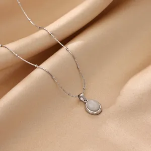 Close-up detail of a minimalist oval cat eye stone pendant necklace on smooth gold satin fabric.