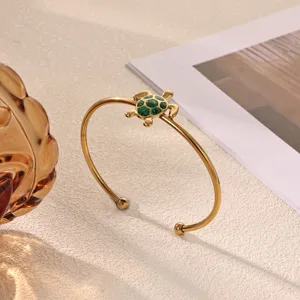 Close-up detail of the gold-plated stainless steel bracelet featuring a green turtle charm.