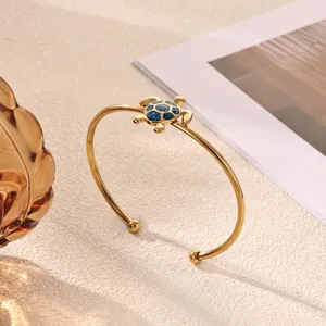Gold-plated open cuff bracelet featuring a detailed blue glitter turtle charm detail shot.
