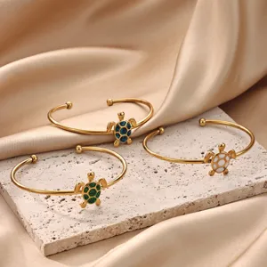 Close-up of golden turtle cuff bracelets featuring sparkling shell details on stone slab background.