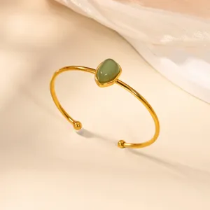 Close-up detail of a minimalist gold stainless steel open cuff bracelet with a green stone.