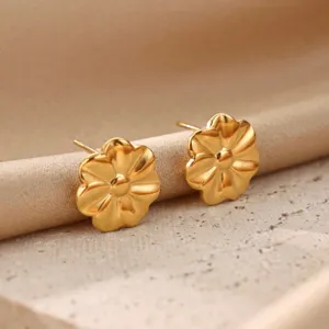 Close-up of golden flower stud earrings on satin and stone background, exquisite detail showcase.