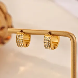 Close-up detail of gold-tone huggie hoop earrings embedded with sparkling crystals.