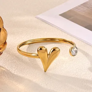 Close-up of gold stainless steel open bangle bracelet with heart charm and clear rhinestone.