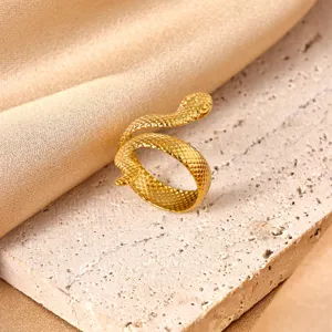 Close-up detail of a stylish gold snake ring resting on a textured stone surface with silk drape.