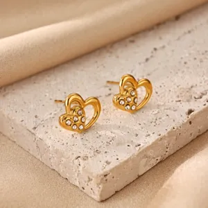 Gold heart stud earrings with sparkling rhinestones displayed on chic stone block main view.