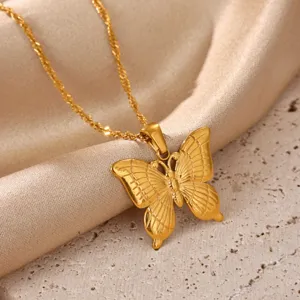Close-up of a gold-plated butterfly pendant necklace on textured silk and stone background.