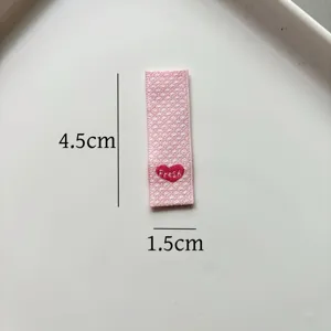 Vista dettagliata dell'etichetta tessuta rosa con ricamo a cuore per cucito fai da te.