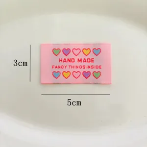 Vue détaillée de l'étiquette tissée rose avec des cœurs colorés et du texte fait main pour vêtements.