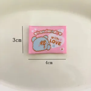Vue détaillée d'une étiquette tissée rose avec motif d'ours et texte d'amour, taille 3x4 cm.