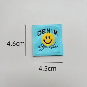 Close-up detail shot of a blue woven patch featuring a yellow smiley face and denim text.