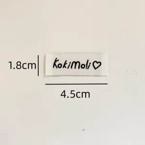 Custom sewing label detail closeup, white woven cloth tag with cute black text and heart logo.
