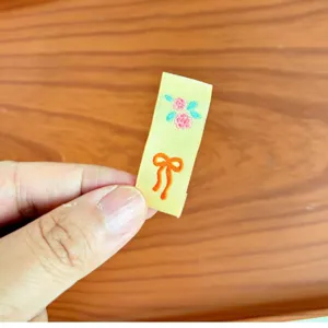 Etichetta tessuta con grazioso ricamo di rosa e fiocco arancione per abbigliamento e scarpe.