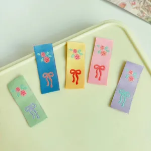 Dettaglio in primo piano di etichette in tessuto colorato con delicati motivi ricamati a rosa e fiocco.