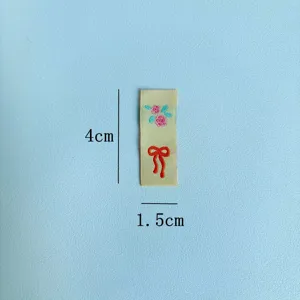 Etichetta in tessuto con ricamo floreale e fiocco, vista dettagliata per accessori di abbigliamento.